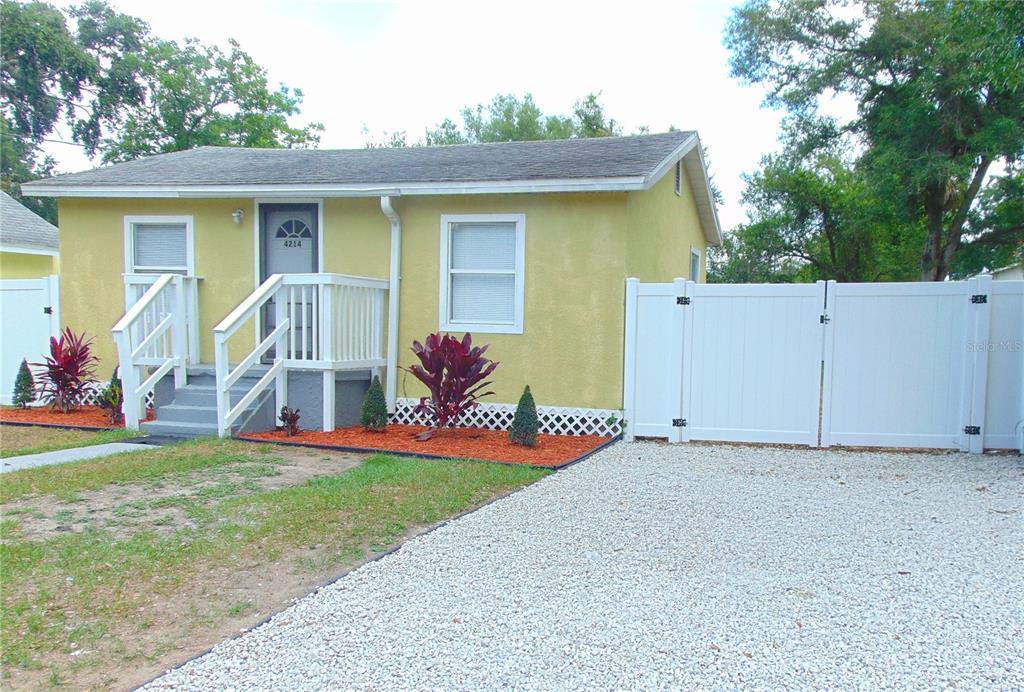 A yellow single-story house features a white front porch, gravel driveway, and white vinyl fencing — 4214 E PALIFOX STREET, TAMPA, FL