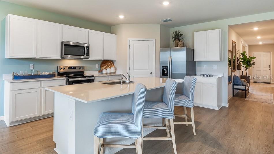 A kitchen features white cabinets, stainless steel appliances, a quartz island, and light wood flooring — 17615 WHISKEY CREEK TRAIL, PARRISH, FL
