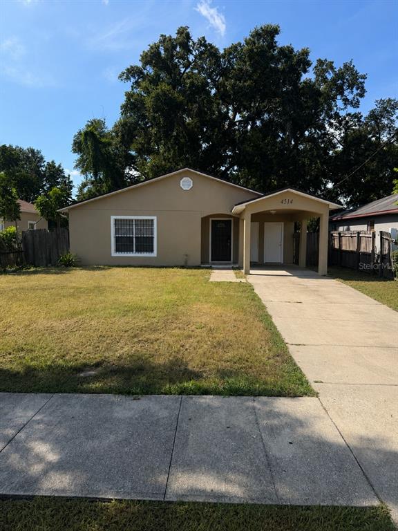 A single-story house with a beige exterior, a front carport, and a large tree behind it — 4514 CYPRESS STREET, ORLANDO, FL