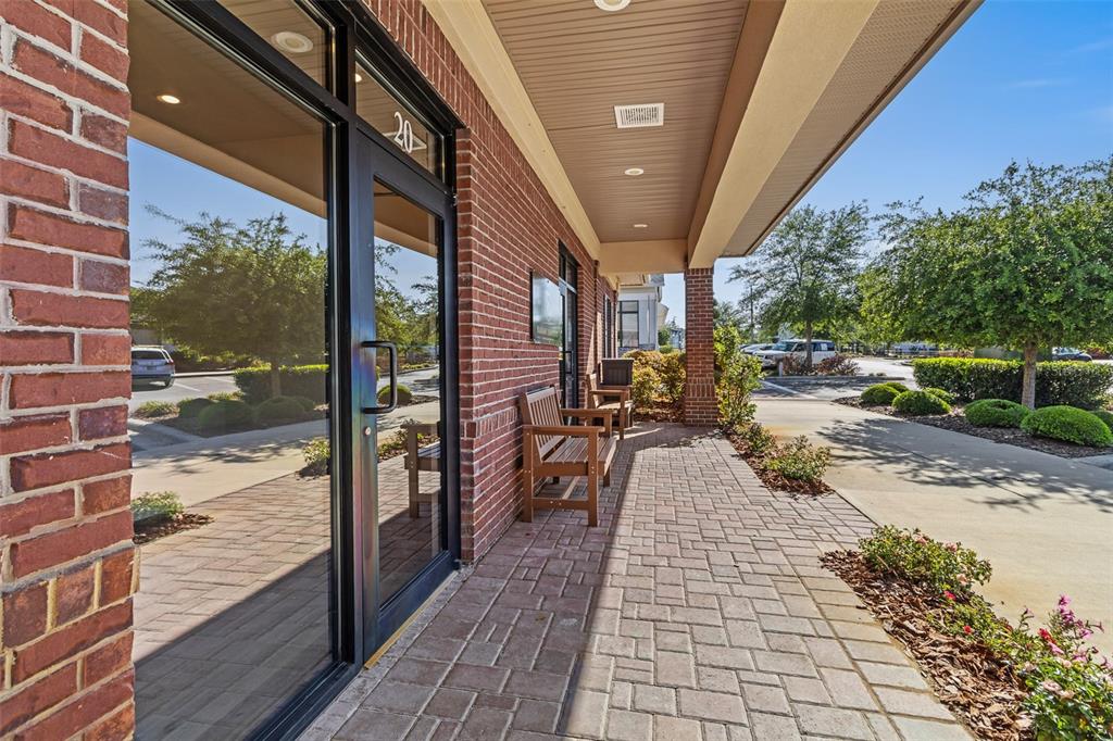A brick building exterior features a glass door, a covered walkway, and wooden benches — 13576 NW 2ND LANE UNIT 20, NEWBERRY, FL