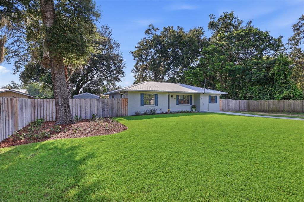 A single-story house with a light-colored exterior, metal roof, and blue shutters sits on grass — 115 NE 5TH STREET, CHIEFLAND, FL