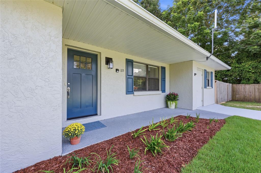 A front porch with a blue door, a window with blue shutters, and a garden bed — 115 NE 5TH STREET, CHIEFLAND, FL