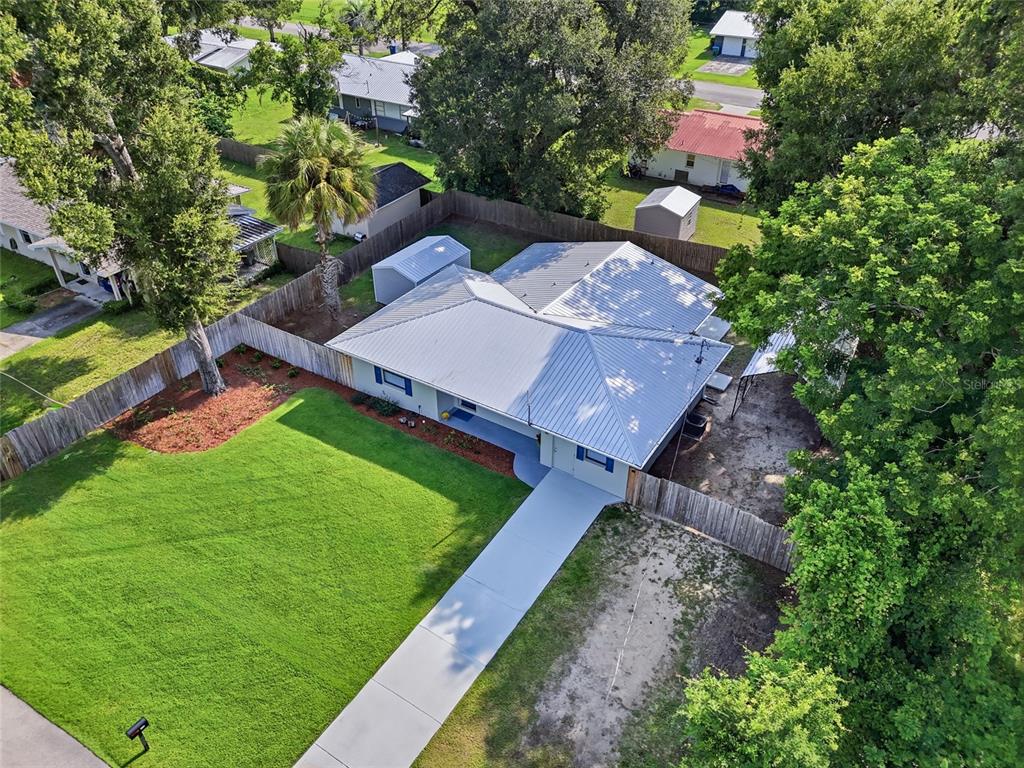 An aerial view shows a single-story house with a metal roof and a concrete driveway — 115 NE 5TH STREET, CHIEFLAND, FL
