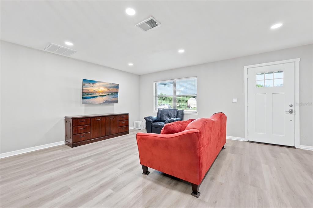 A living room features light wood-look flooring, a red sofa, a dark armchair, and a television — 115 NE 5TH STREET, CHIEFLAND, FL
