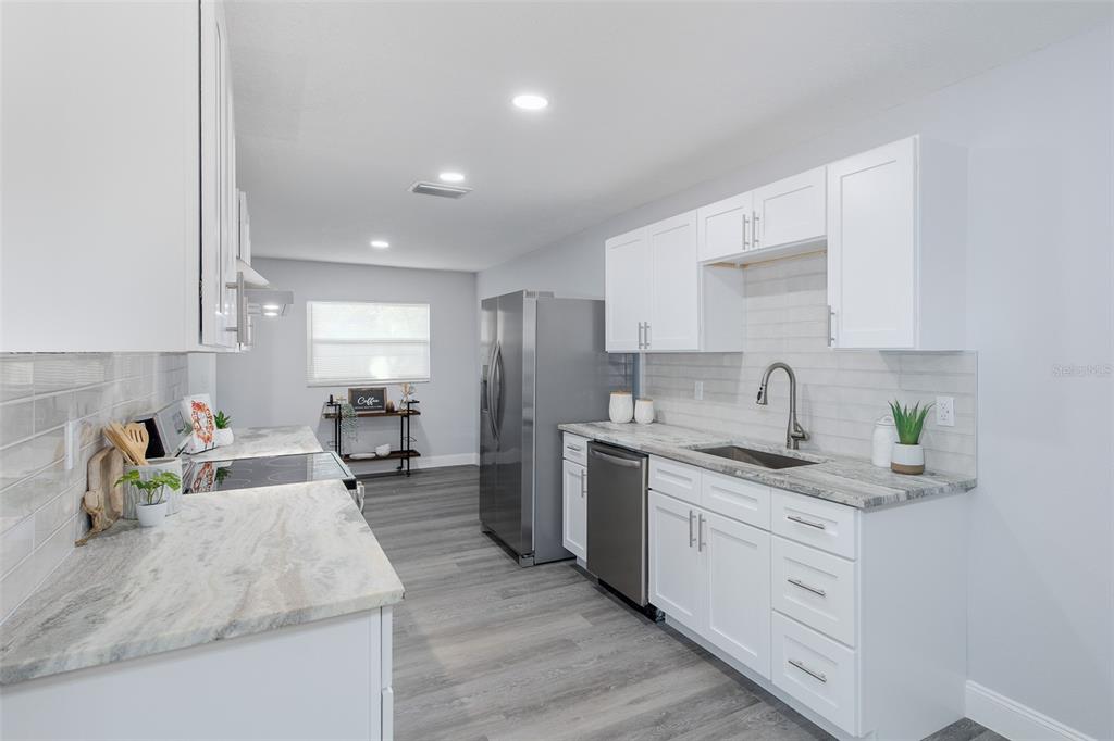 A modern kitchen features white cabinets, stone countertops, stainless steel appliances, and gray wood flooring — 1815 DRIFTWOOD CIRCLE S, OLDSMAR, FL