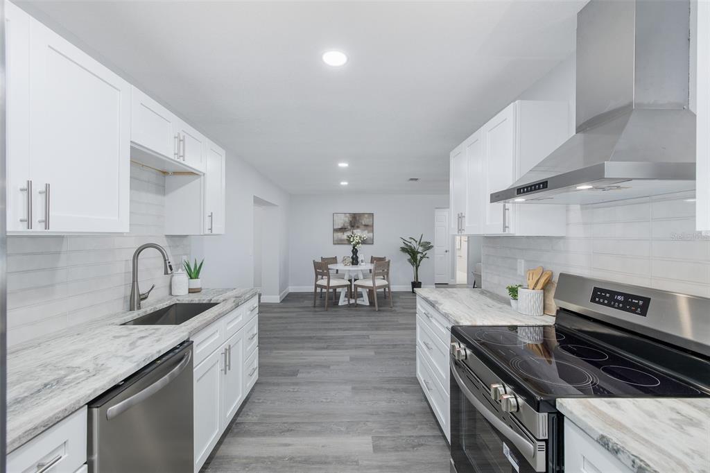 A galley kitchen with white cabinets, marble-look countertops, and stainless steel appliances leads to dining — 1815 DRIFTWOOD CIRCLE S, OLDSMAR, FL