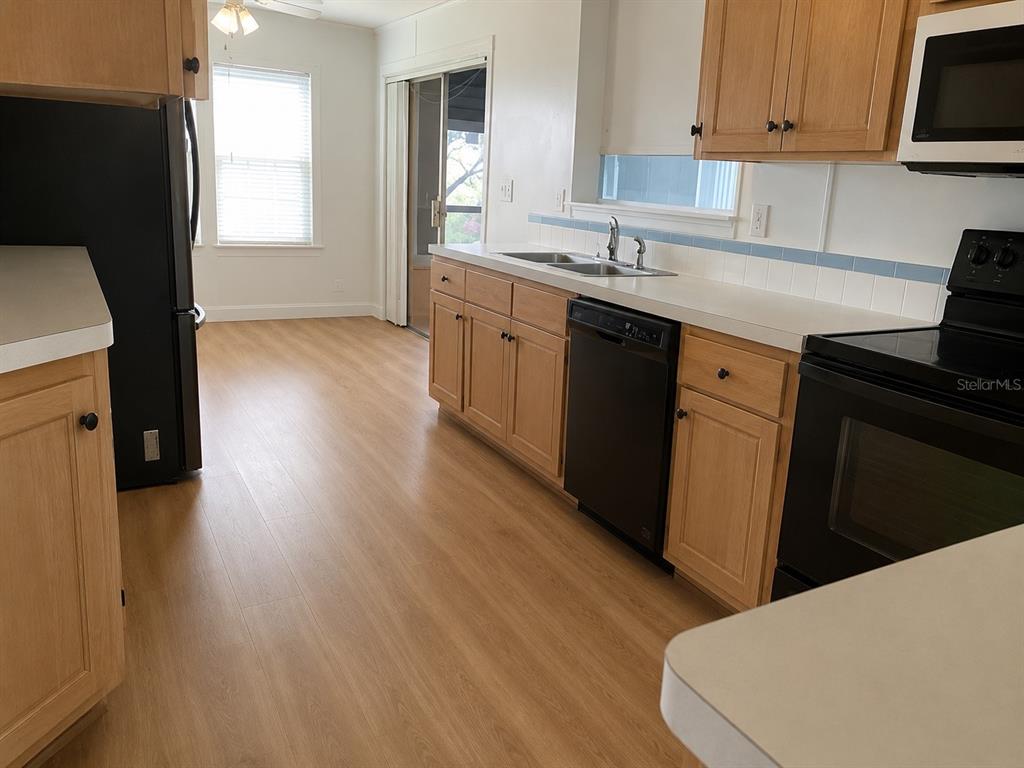 A kitchen features light wood cabinets, black appliances, white countertops, and light-colored wood-look flooring — 37643 LANDIS AVENUE, ZEPHYRHILLS, FL