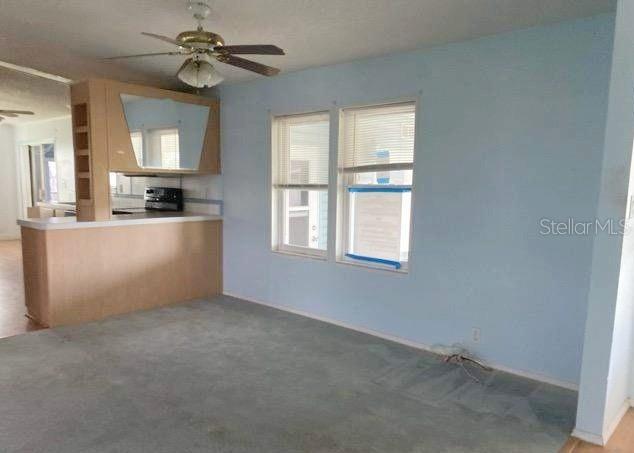 A room with light blue walls, gray carpeting, a ceiling fan, and a kitchen pass-through counter — 37643 LANDIS AVENUE, ZEPHYRHILLS, FL