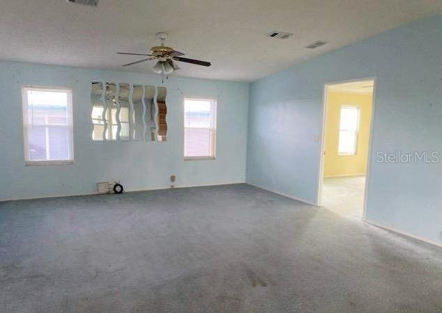 A spacious room with light blue walls, gray carpeting, a ceiling fan, and mirrored wall panels — 37643 LANDIS AVENUE, ZEPHYRHILLS, FL