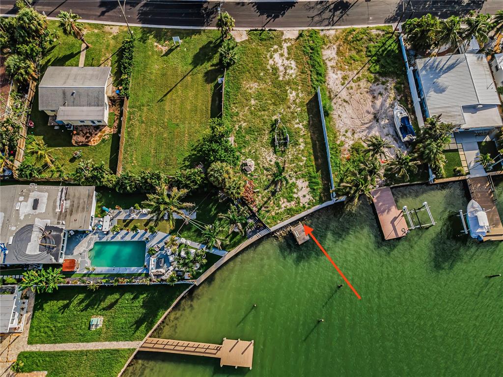 An aerial view shows a vacant waterfront lot with a small dock and a red arrow — 14035 E PARSLEY DRIVE, MADEIRA BEACH, FL