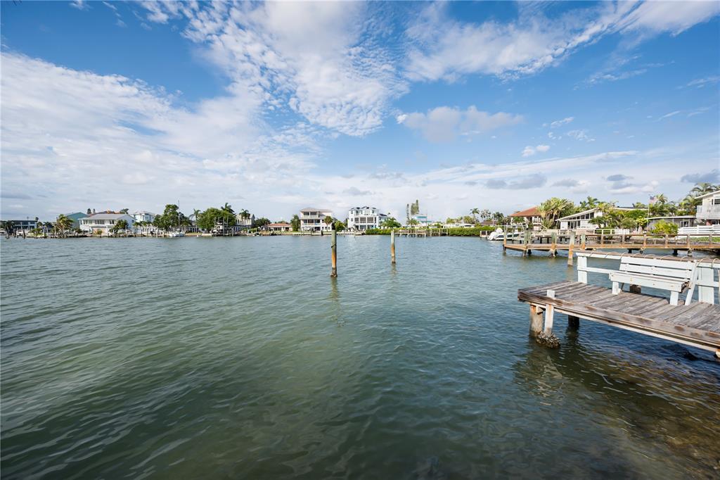 A wooden dock with a bench extends into a calm waterway lined with waterfront homes — 14035 E PARSLEY DRIVE, MADEIRA BEACH, FL