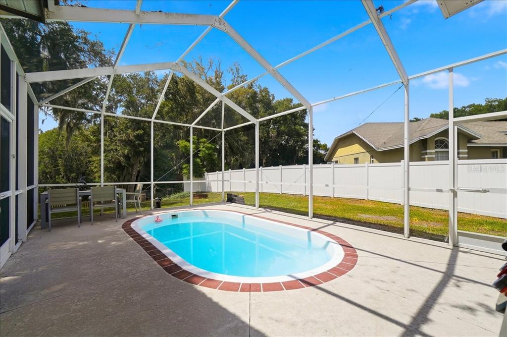 An oval swimming pool sits on a concrete patio inside a screened-in pool enclosure — 448 LAKE HARRIS DRIVE, LAKELAND, FL