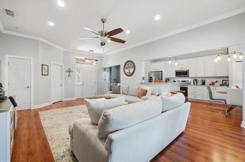 An open-concept living room with wood floors, a ceiling fan, and an adjacent white kitchen — 448 LAKE HARRIS DRIVE, LAKELAND, FL
