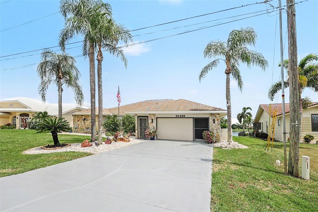 A living room features wood-look flooring, a gray sofa, a surfboard coffee table, and a ceiling fan — 25426 SAINT HELENA LANE, PUNTA GORDA, FL