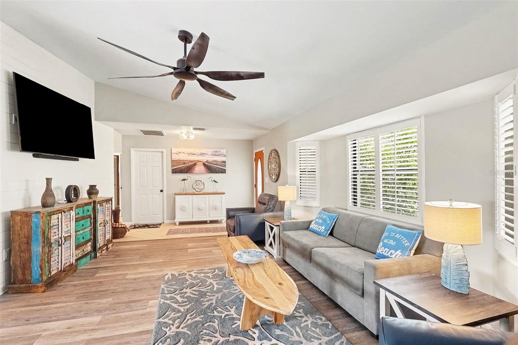 A living room features wood-look flooring, a vaulted ceiling, a leather armchair, and a television — 25426 SAINT HELENA LANE, PUNTA GORDA, FL