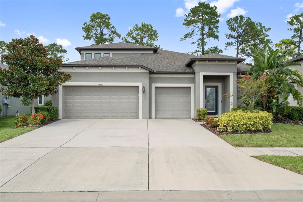 A gray, two-story suburban house features a three-car garage and a landscaped front yard — 18565 OBREGAN DRIVE, SPRING HILL, FL