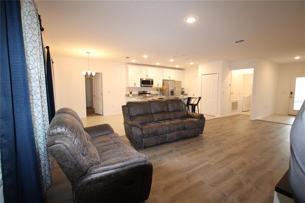 An open-concept living room with wood-look flooring leads into a kitchen with white cabinets — 516 INGLESIDE LANE, HAINES CITY, FL