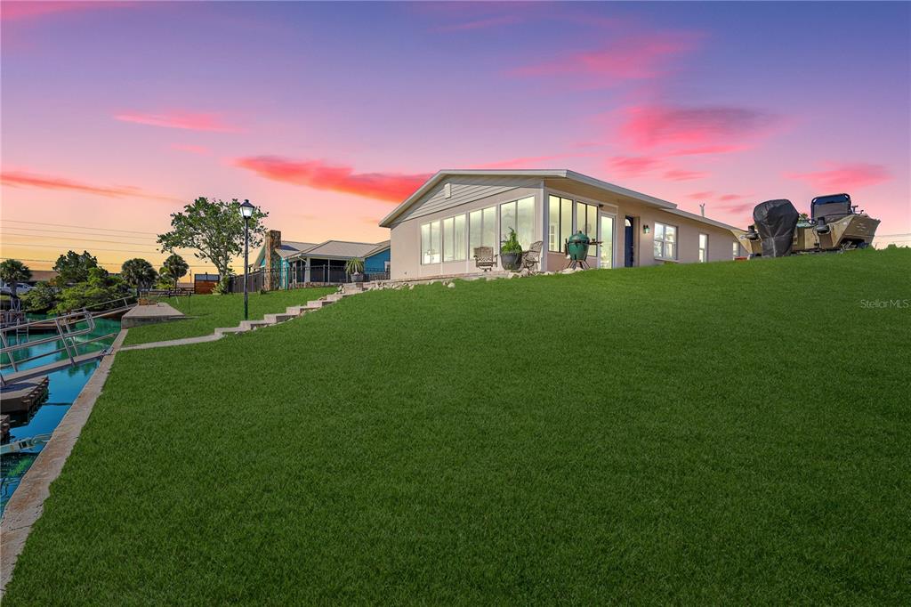 A house with a large sunroom sits on a grassy hill overlooking a canal — 4392 3RD ISLE DRIVE, HERNANDO BEACH, FL