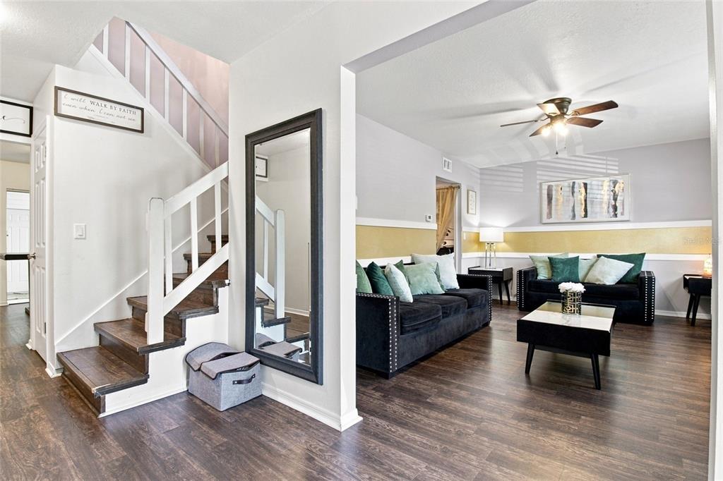 A living room with dark wood floors, black sofas, and a staircase with a wall mirror — 3039 ABBEY COURT, CLEARWATER, FL
