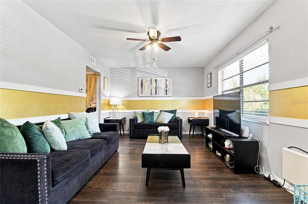 A living room features dark sofas, a coffee table, a television, and yellow wall accents — 3039 ABBEY COURT, CLEARWATER, FL