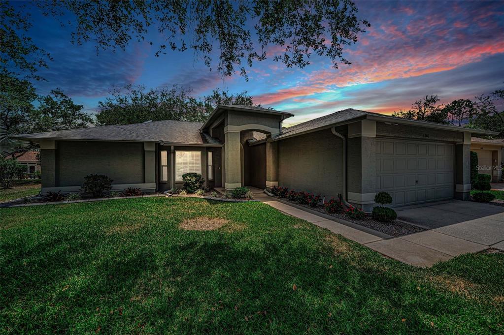 A single-story house with a gray exterior, a two-car garage, and a sunset sky — 1300 FALLOWFIELD DRIVE, TRINITY, FL