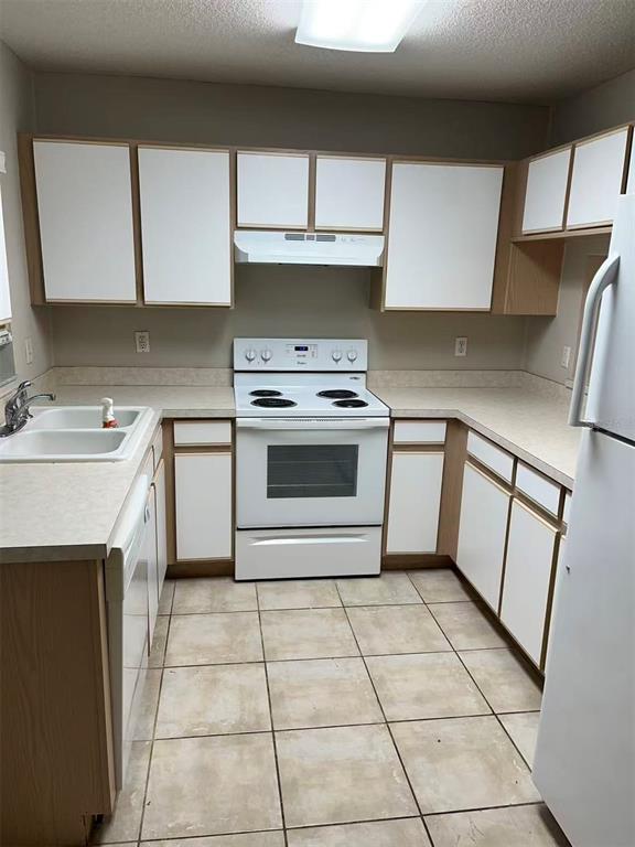 A kitchen features white cabinets, a white electric stove, and light-colored tile flooring — 2030 FLUORSHIRE DRIVE, BRANDON, FL