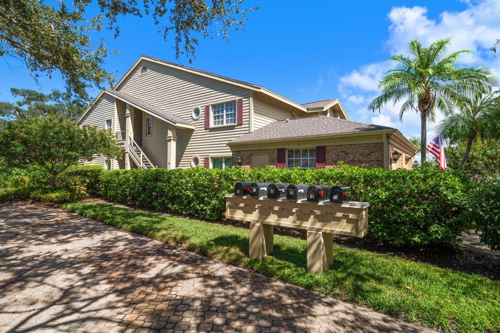 A row of black mailboxes stands in front of a two-story tan building with landscaping — 75 PELICAN PLACE, BELLEAIR, FL