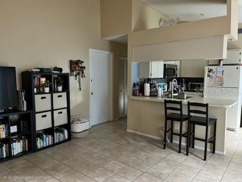 A living room with a bookshelf and a kitchen with a breakfast bar and stools — 516 SHERIDAN DRIVE, PALM HARBOR, FL