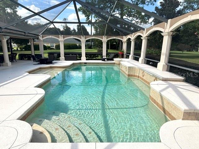 A screened-in swimming pool with a sun shelf and steps sits on a paved patio — 1701 TIMBER EDGE DRIVE, DELAND, FL