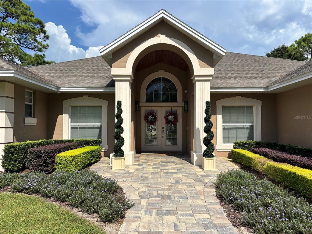 The exterior of a house features a stone walkway leading to a double-door arched entrance — 1701 TIMBER EDGE DRIVE, DELAND, FL