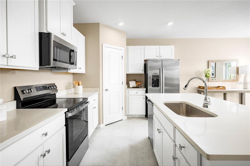 A modern kitchen features white cabinets, stainless steel appliances, a center island, and tile flooring — 11448 SE 77TH AVENUE, BELLEVIEW, FL