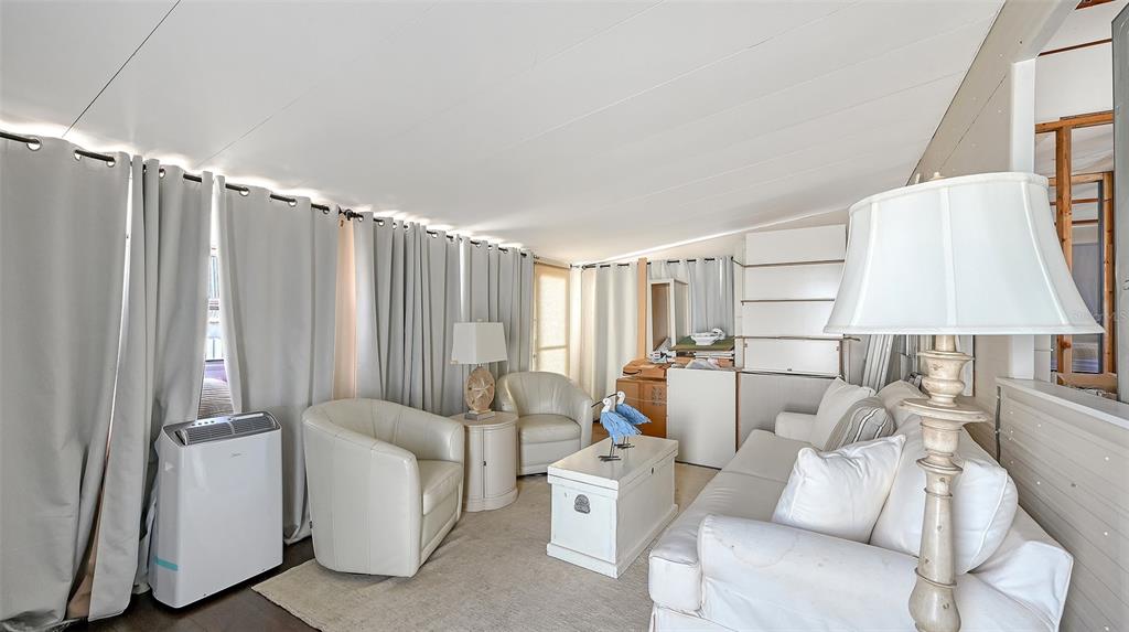 A sunroom features white furniture, a portable air conditioner, and floor-to-ceiling curtains — 36 TWIN SHORES BOULEVARD, LONGBOAT KEY, FL