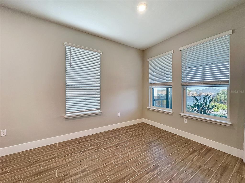 An empty room features wood-look tile flooring, light gray walls, and three windows with blinds — 651 CONSERVATION BOULEVARD, GROVELAND, FL