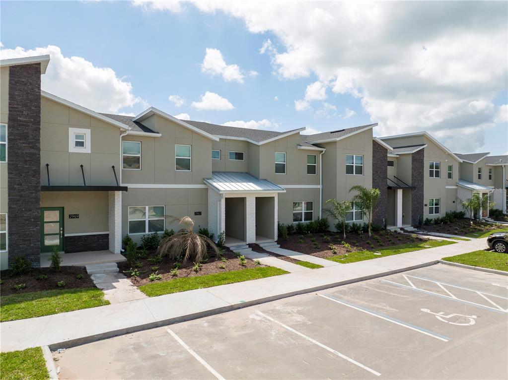 A row of modern two-story townhouses features tan siding, stone accents, and a paved parking lot — 2967 PENELOPE LOOP, KISSIMMEE, FL