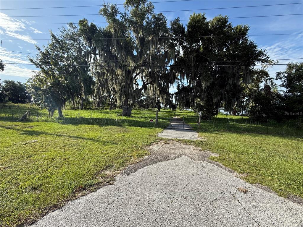 A gravel driveway leads to a gated entrance on a grassy lot with large trees — US HIGHWAY 17/92 W, HAINES CITY, FL