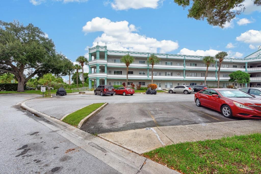 A multi-story apartment building with a parking lot in the foreground under a blue sky — 2370 JAMAICAN STREET UNIT 30, CLEARWATER, FL