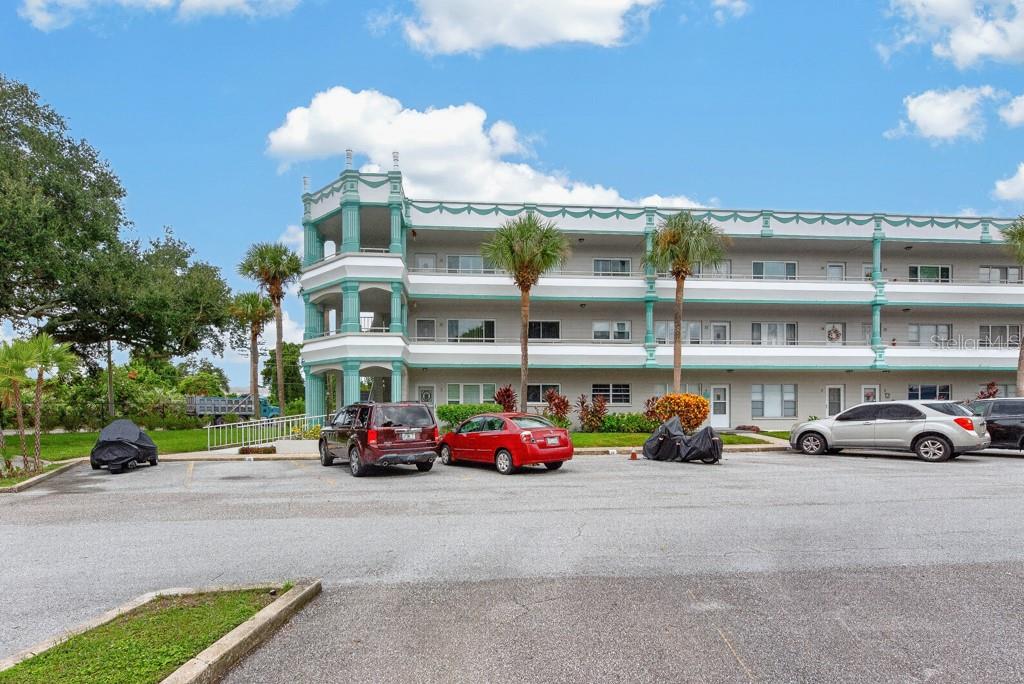 A three-story apartment building with teal accents and a parking lot in the foreground — 2370 JAMAICAN STREET UNIT 30, CLEARWATER, FL
