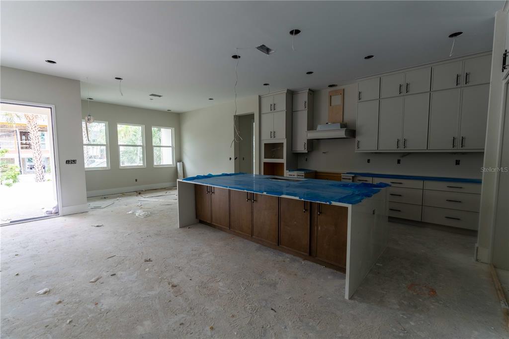 An unfinished kitchen features a large center island, light-colored cabinetry, and a sliding glass door — 4906 W ESTRELLA STREET, TAMPA, FL
