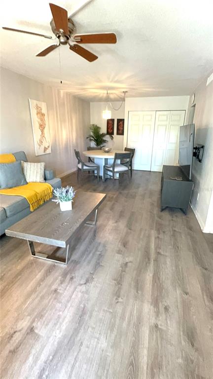 A living room with wood-look flooring, a gray sofa, a coffee table, and a dining area — 1799 N HIGHLAND AVENUE UNIT 75, CLEARWATER, FL