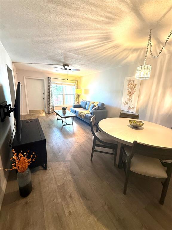 An open-concept living and dining area features wood-look flooring, a gray sofa, and a round table — 1799 N HIGHLAND AVENUE UNIT 75, CLEARWATER, FL