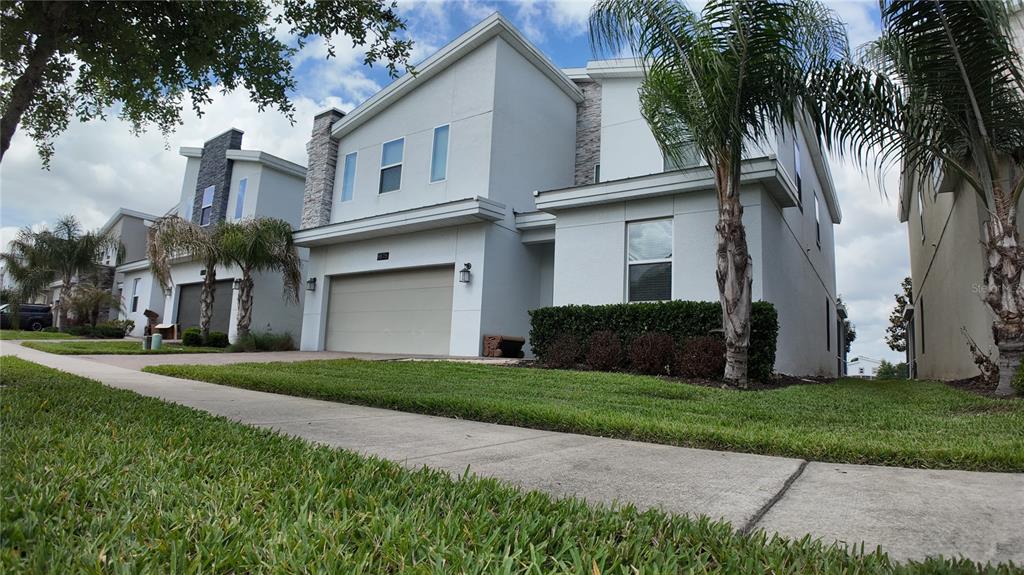A two-story modern house with a light gray exterior, a two-car garage, and palm trees — 8876 CABOT CLIFFS DRIVE, DAVENPORT, FL