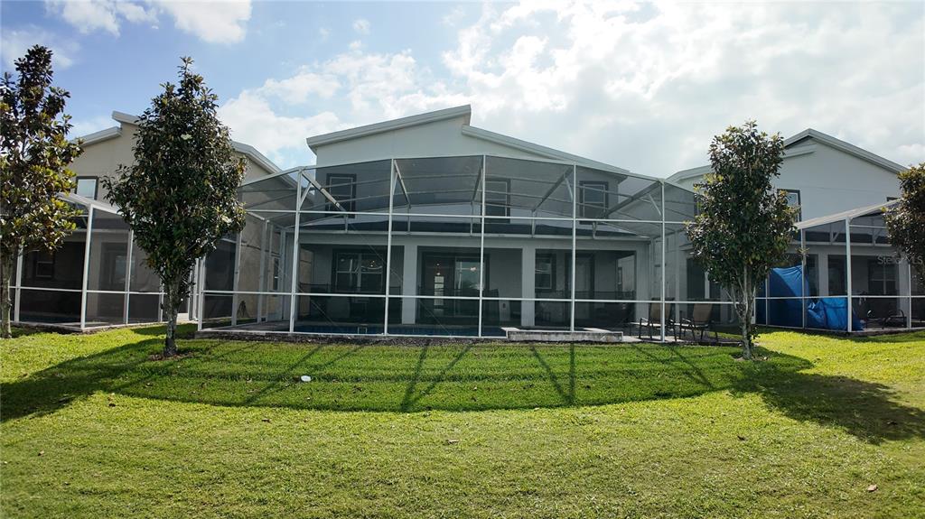 The exterior of a two-story house features a screened-in pool area and a grassy backyard — 8876 CABOT CLIFFS DRIVE, DAVENPORT, FL