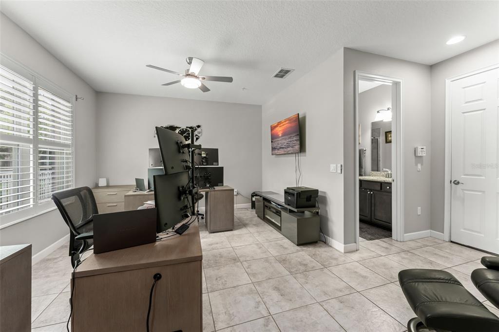 A home office features two desks with multiple computer monitors, tile flooring, and a ceiling fan — 1457 LAKE GEORGE DRIVE UNIT 1457, LAKE MARY, FL