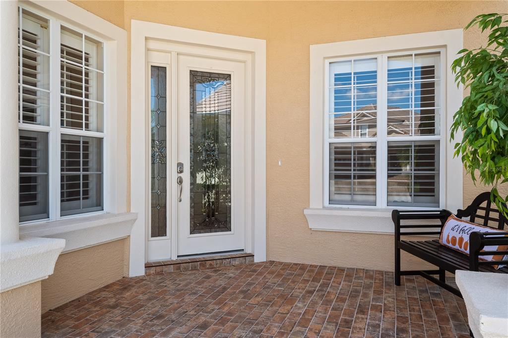 A front porch with a decorative glass door, two windows, and a black wooden bench — 2464 LAUREL GLEN DRIVE, LAKELAND, FL