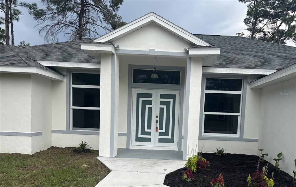 The exterior of a single-story house features a white stucco facade, gray trim, and double doors — 6807 SW 148TH PLACE ROAD, OCALA, FL