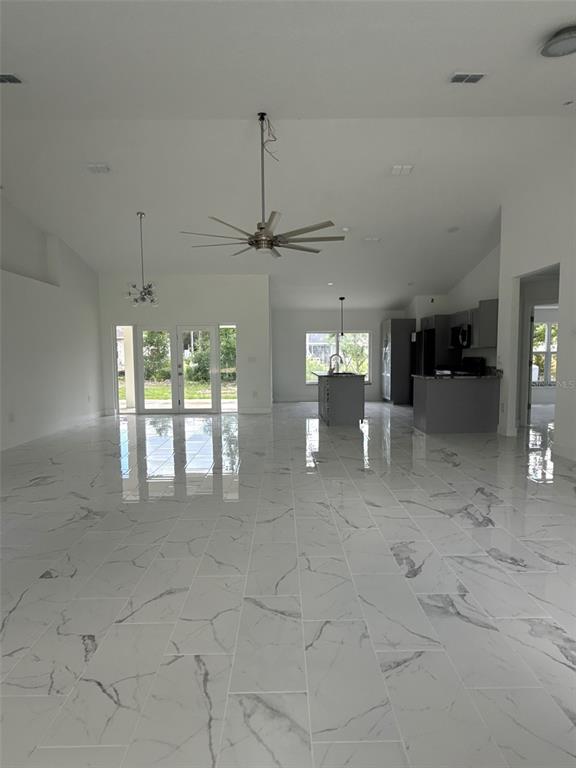 An open-concept living area features white marble-look tile flooring, a ceiling fan, and a kitchen — 6807 SW 148TH PLACE ROAD, OCALA, FL