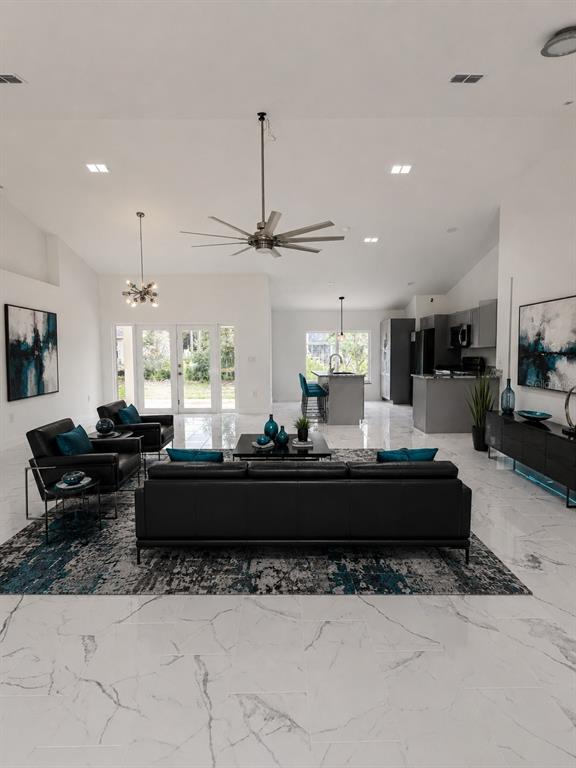 A modern open-concept living room features white marble floors, a black sofa, and vaulted ceilings — 6807 SW 148TH PLACE ROAD, OCALA, FL