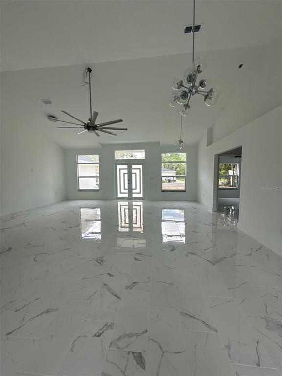 A spacious, bright room features white marble-look tile flooring, a vaulted ceiling, and modern lighting — 6807 SW 148TH PLACE ROAD, OCALA, FL