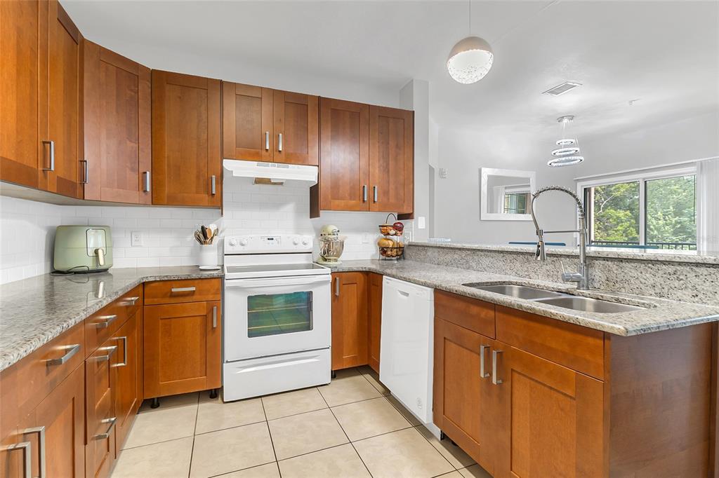 A kitchen features wood cabinets, granite countertops, white appliances, and a tile floor — 1995 ERVING CIRCLE UNIT 208, OCOEE, FL