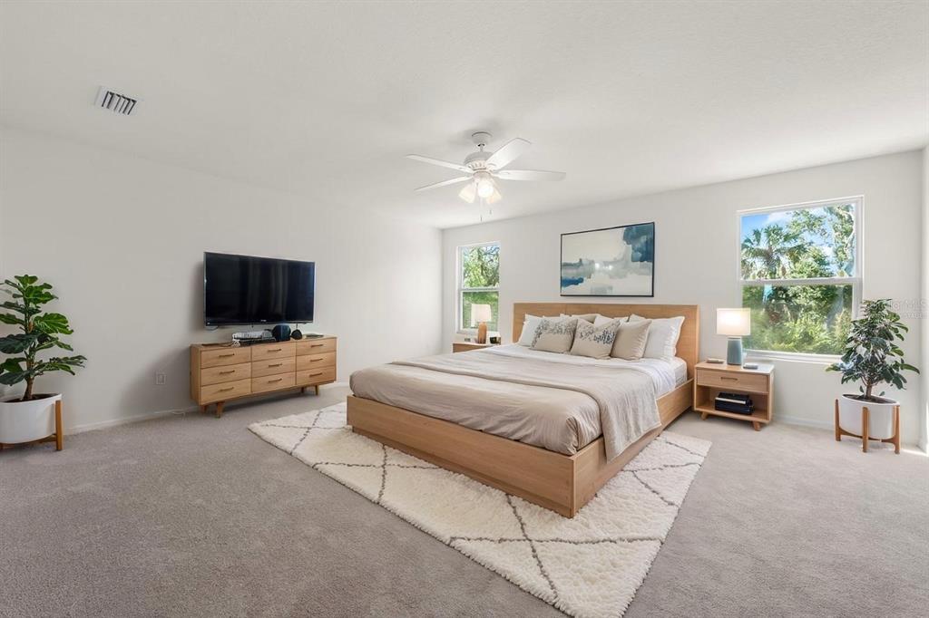 A spacious bedroom features a wooden bed frame, a dresser, and two potted plants — 5715 HEVENA COURT, PALMETTO, FL